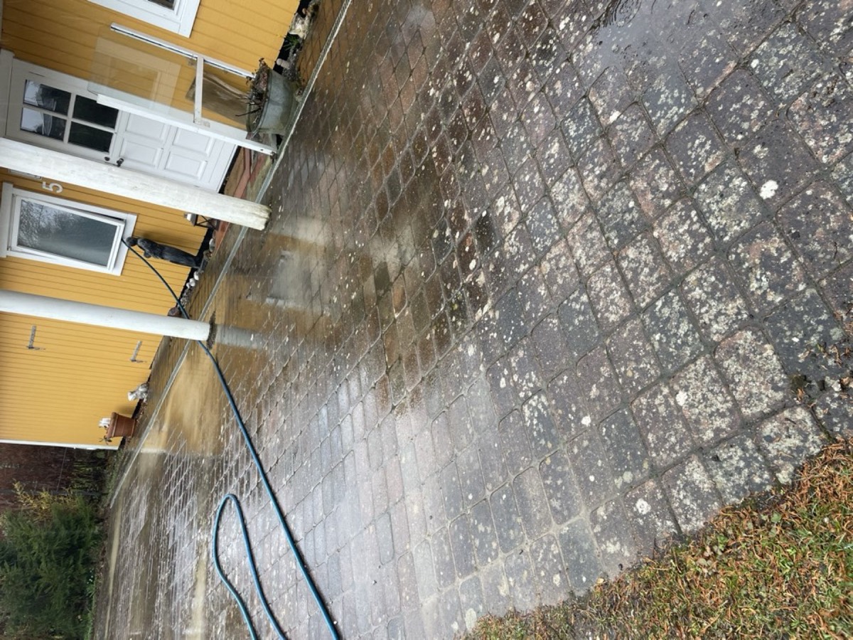 Før: Gårdsplads af røde og grå belægningssten foran et gult hus