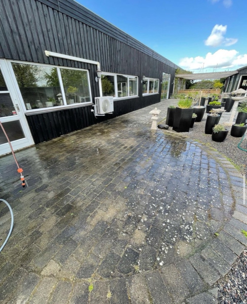 Før: Gårdsplads af grå belægningssten foran en lang, sort bygning