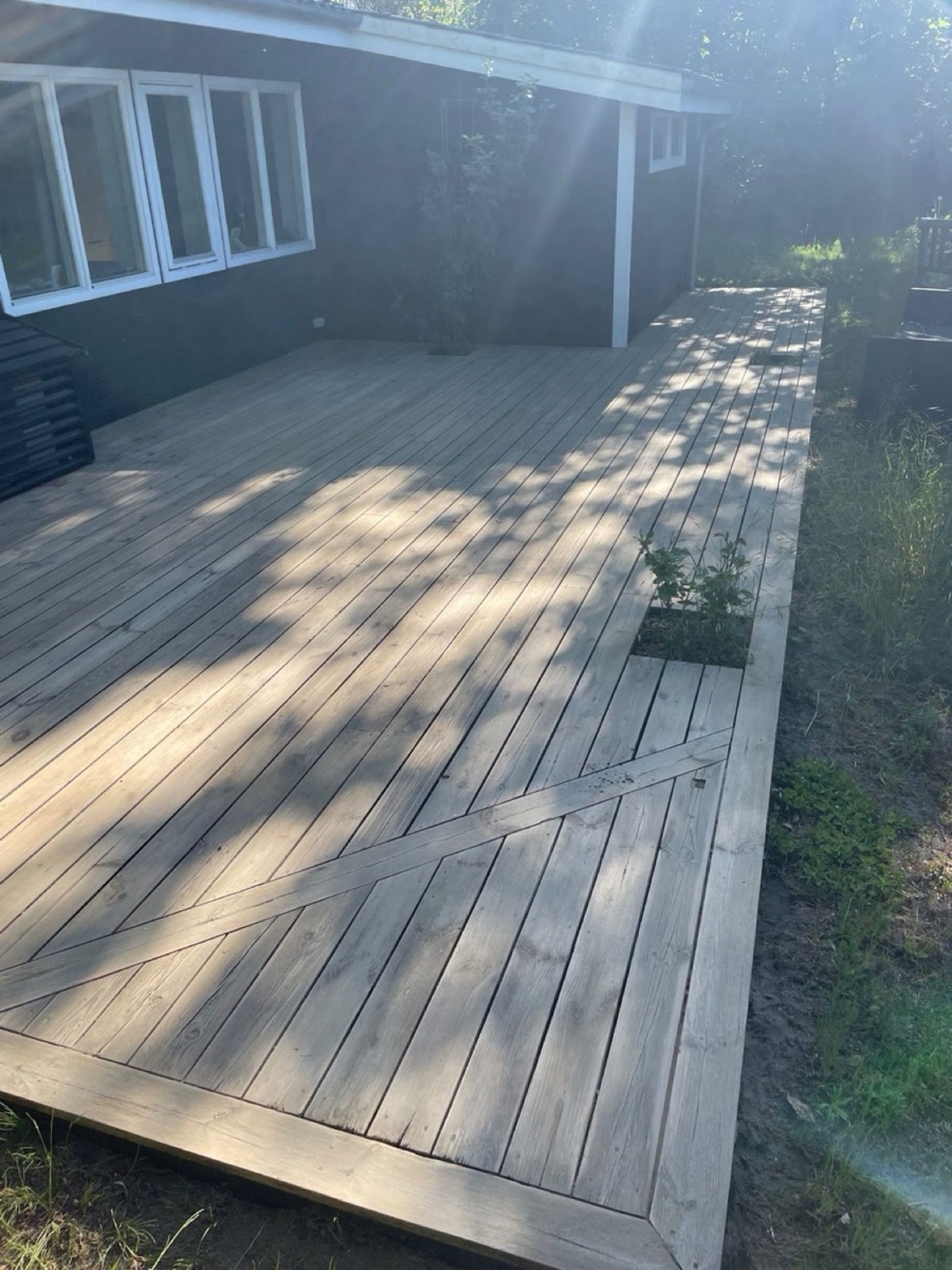 Efter: Træterrasse med diagonalt mønster ved et sort træhus i skoven