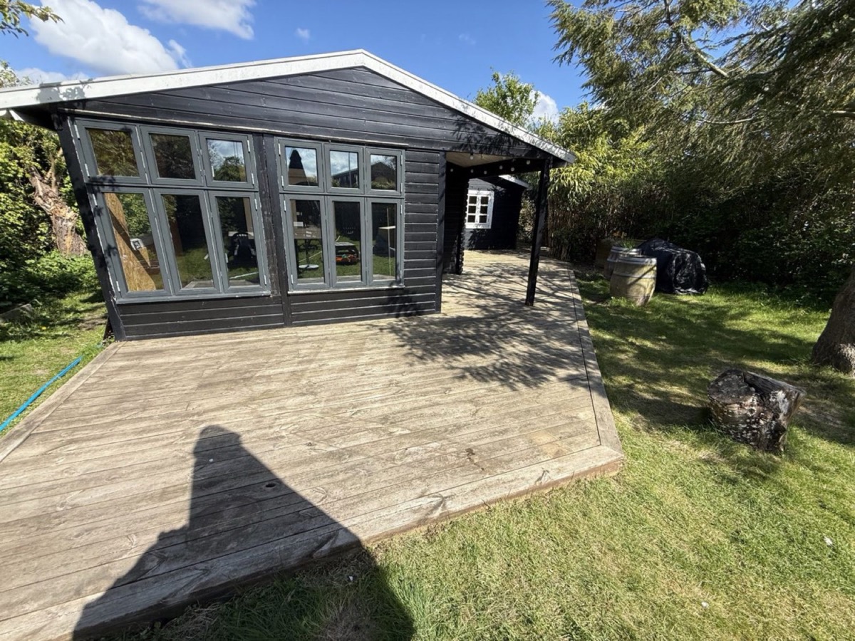 Før: Træterrasse foran et sort sommerhus med sprossevinduer