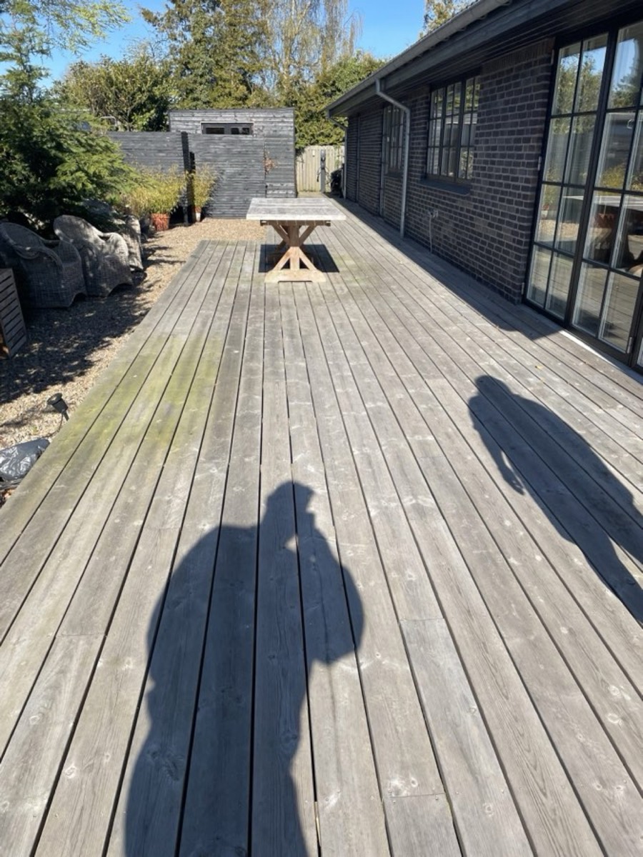 Før: Lang træterrasse langs et sort træhus med store vinduer