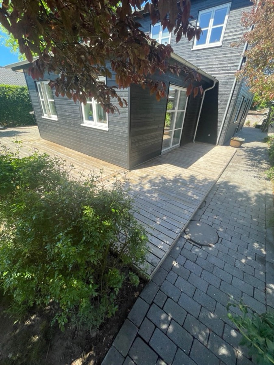 Efter: Træterrasse og belægning omkring et sort anneks