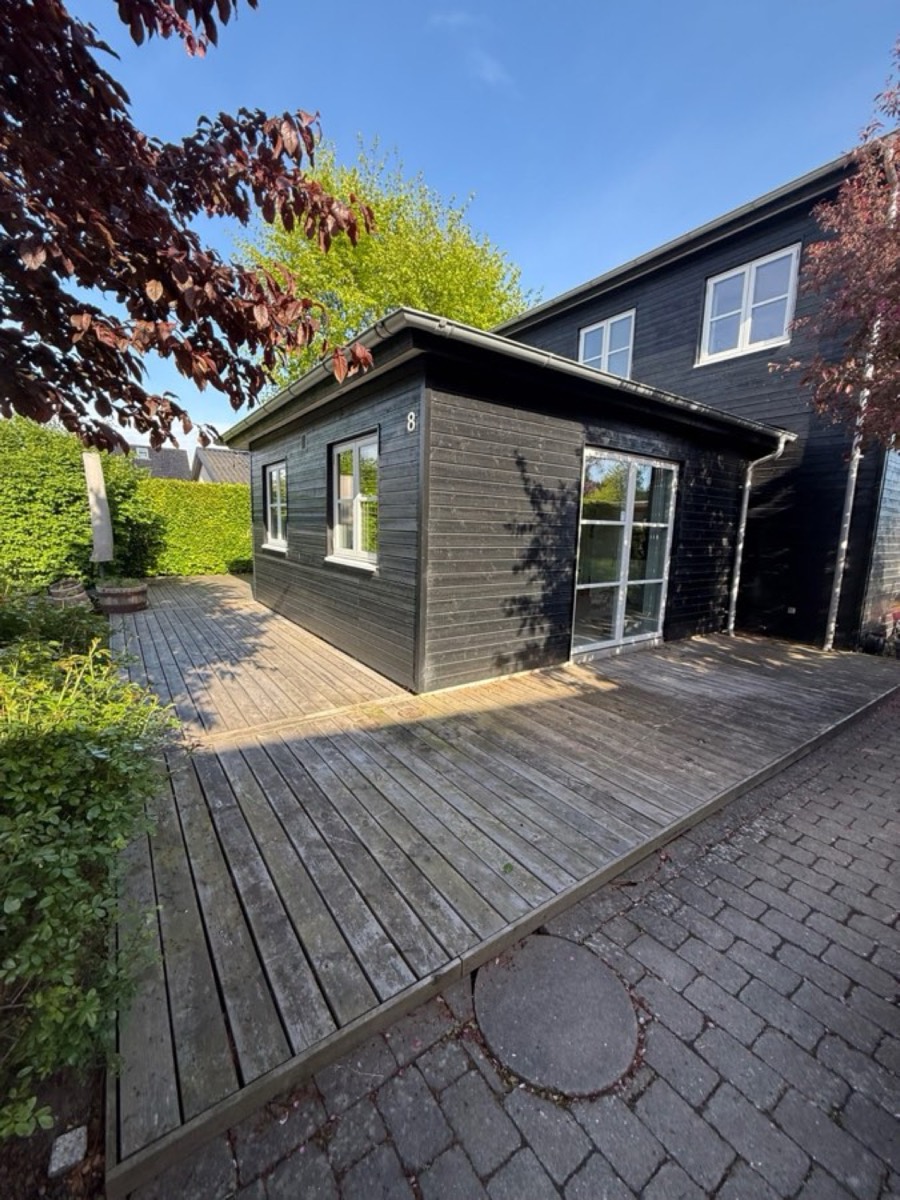 Før: Træterrasse og belægning omkring et sort anneks