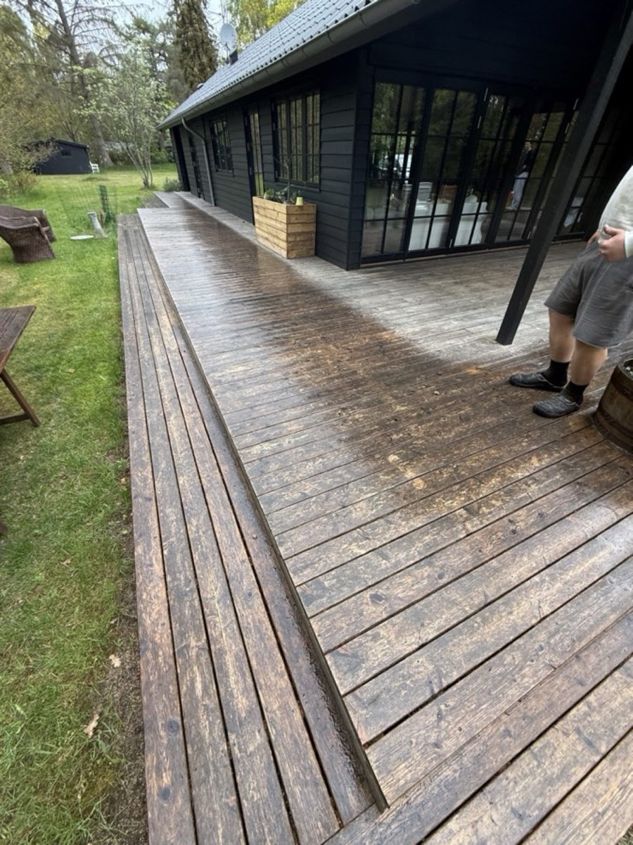 Før: Lang træterrasse i flere niveauer ved et sort hus