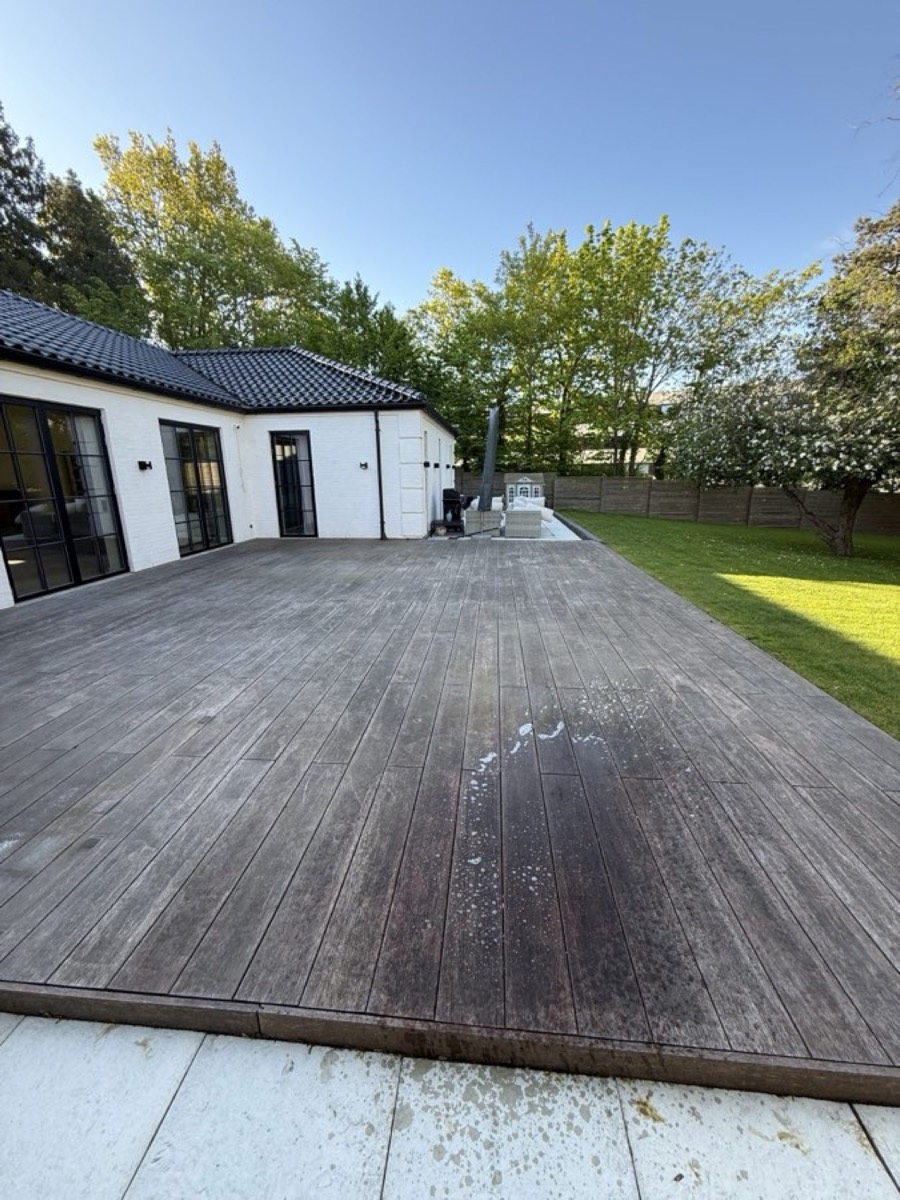 Før: Stor terrasse af hårdttræ ved et hvidt hus med sort tag