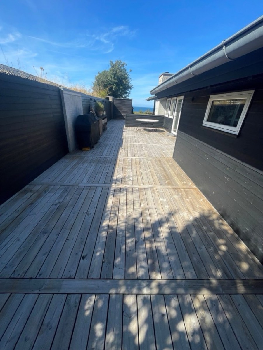 Efter: Lang træterrasse langs et sort sommerhus med havkig