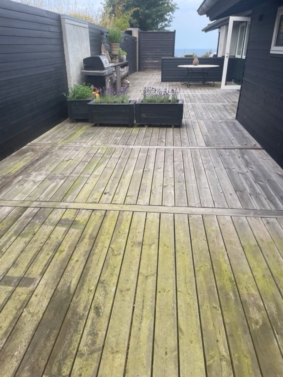 Før: Lang træterrasse langs et sort sommerhus med havkig