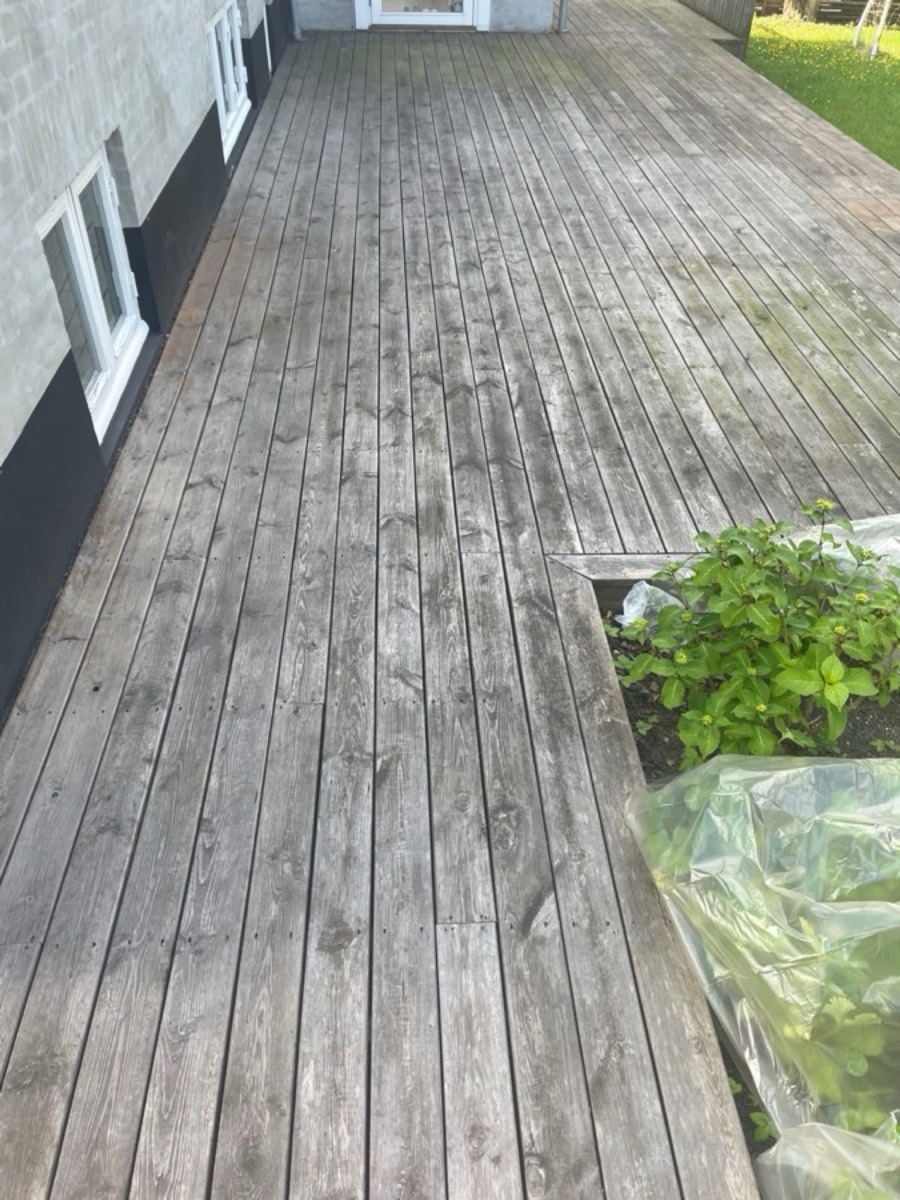 Før: Lang træterrasse langs et hvidt hus med sort sokkel