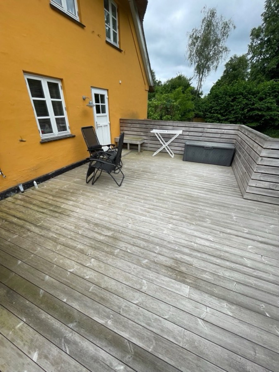 Før: Træterrasse med indbygget bænk ved et gult hus